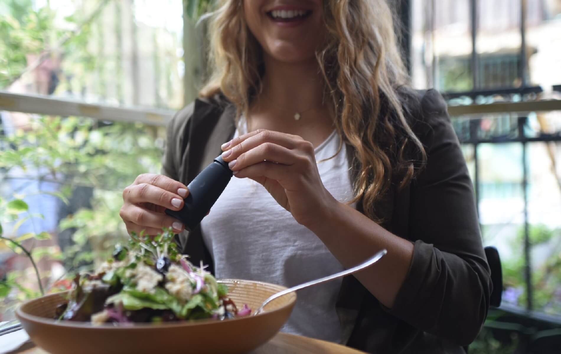 Nutrition - a smiling woman is holding Lumen device, in front of her is a table with a salad